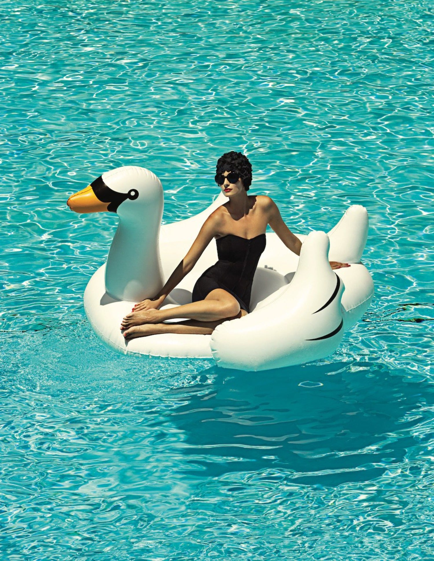 woman floating on swan in swimming pool on a sunny day